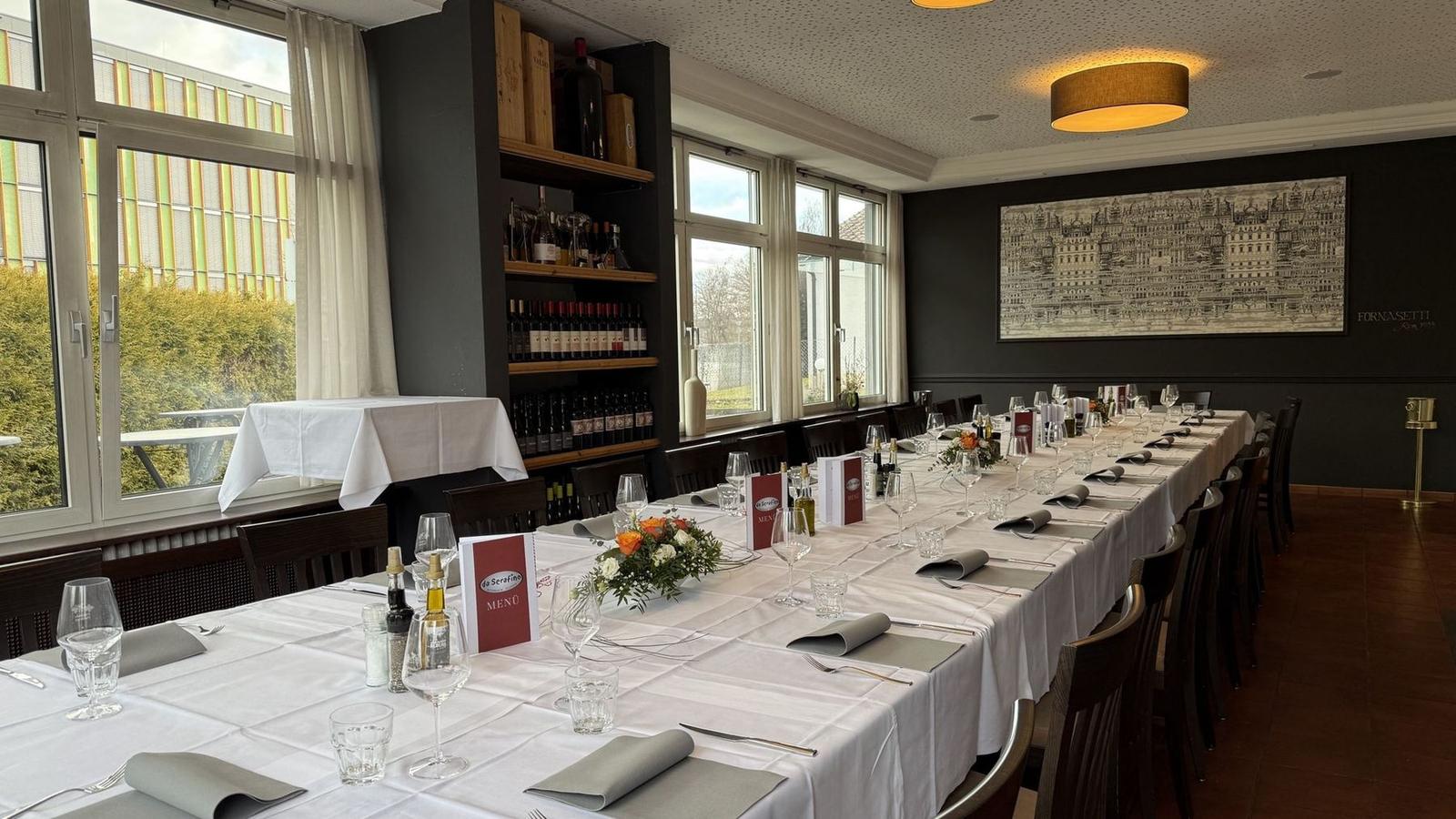 Long festively set table with flower arrangements and da Serafino menu cards in the dining room