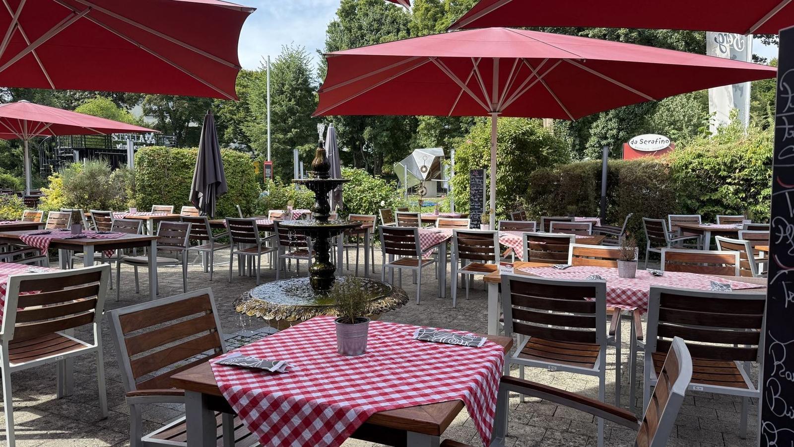 Terrace with a splashing fountain, red parasols and red-and-white checked tablecloths